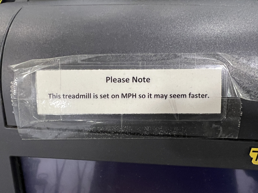 A makeshift sign on a treadmill: “Please Note — This treadmill is set on MPH so it may seem faster.”
